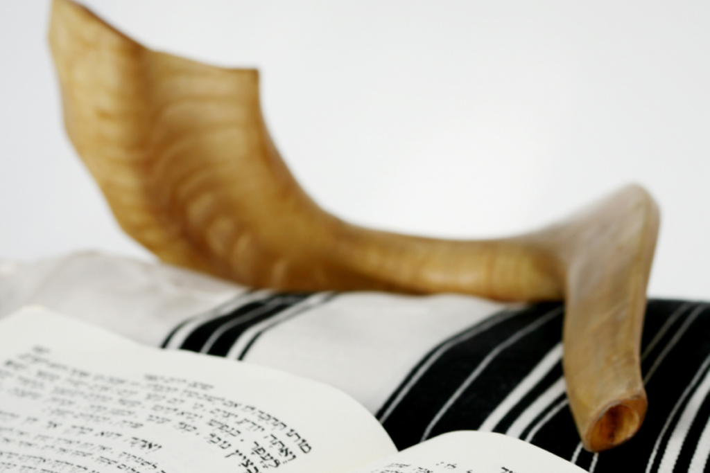 Torah open with a shofar resting atop a tallit.