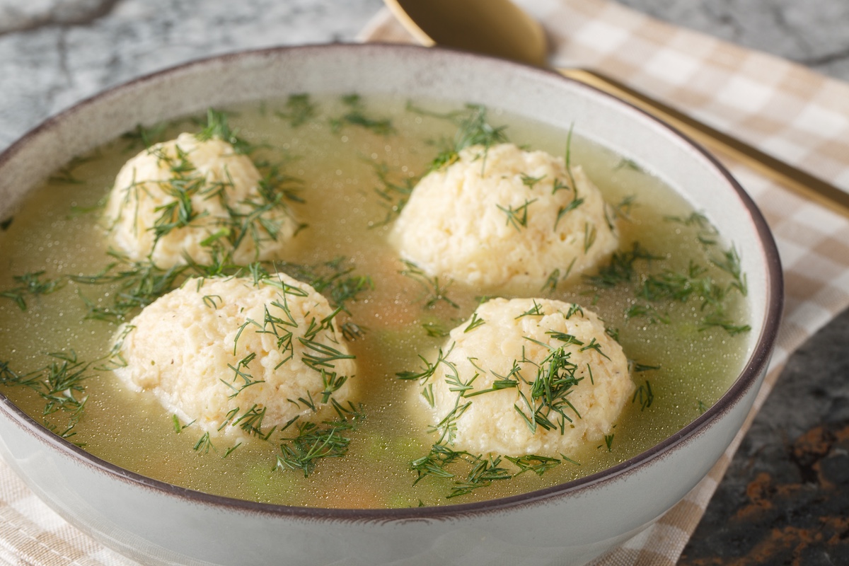 Jewish matzah balls soup with chicken broth, vegetables and dill close-up in a plate on the table.